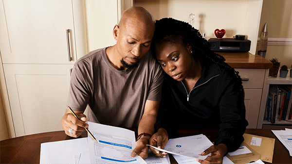 A couple sits at a table, closely reviewing financial documents with a concerned expression.