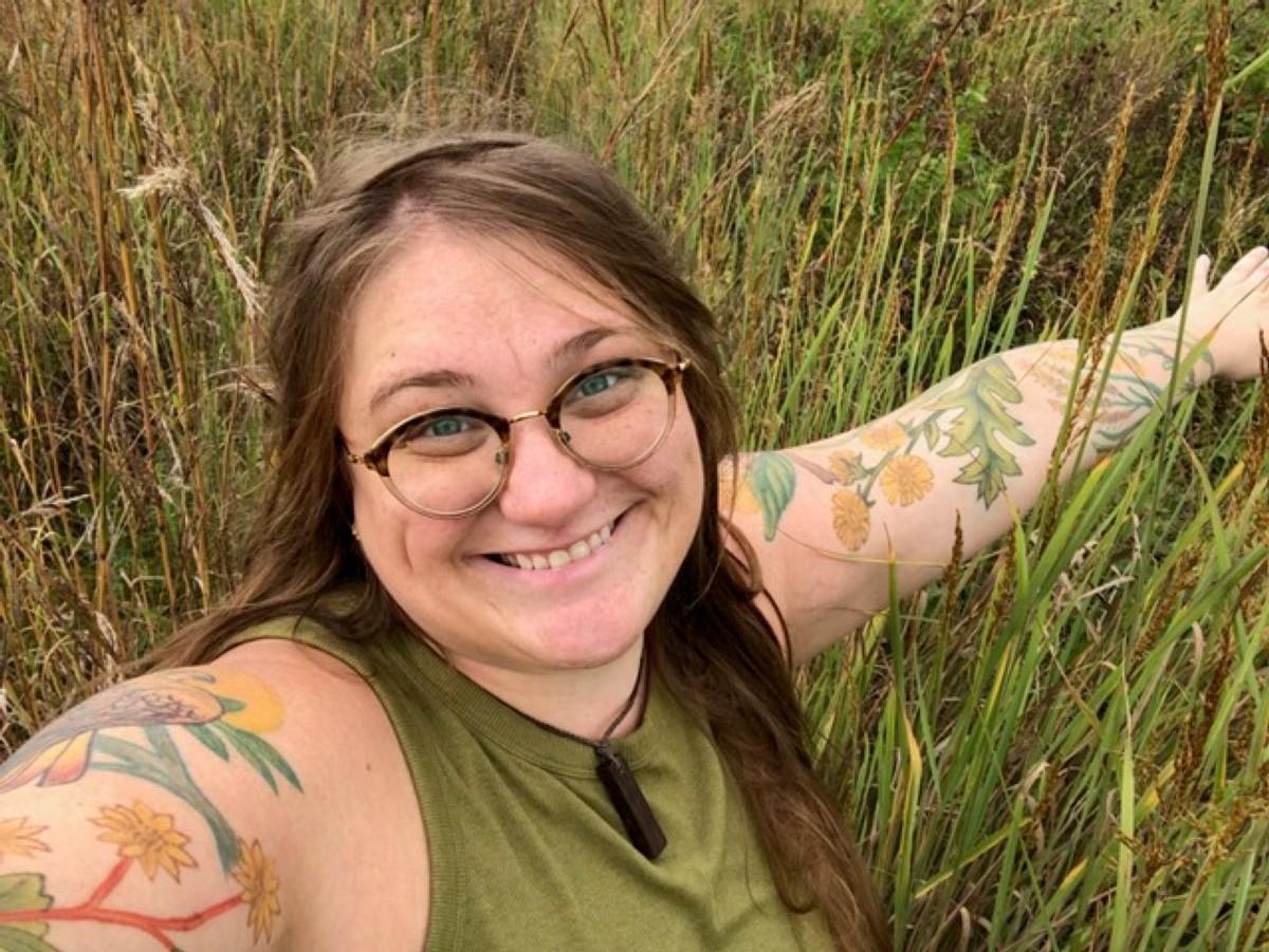 Dr. Liz Anna Kozik with outstretched arms in a meadow