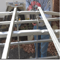 A person using a reciprocating saw to cut the metal bars on the IBC cage.