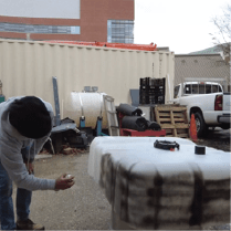 : A person spraying black paint on the outside of the grow bed container.