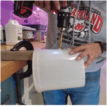 A person is drilling holes into the side of the white plastic mixing container.