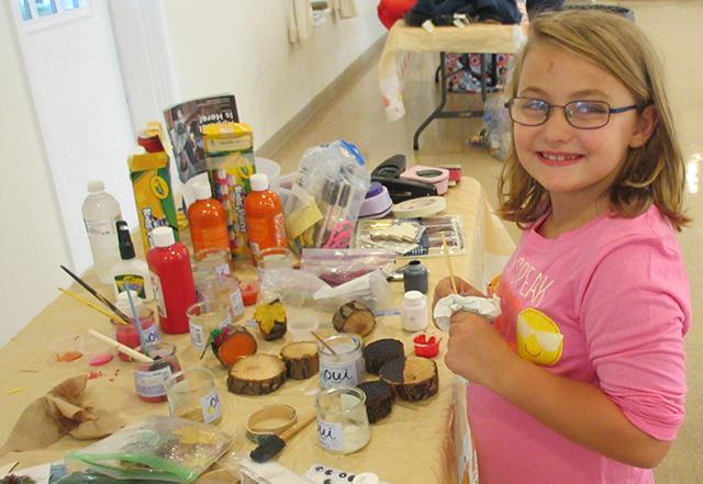 4 H er looks towards camera as they stand in front of table filled with pain and craft supplies