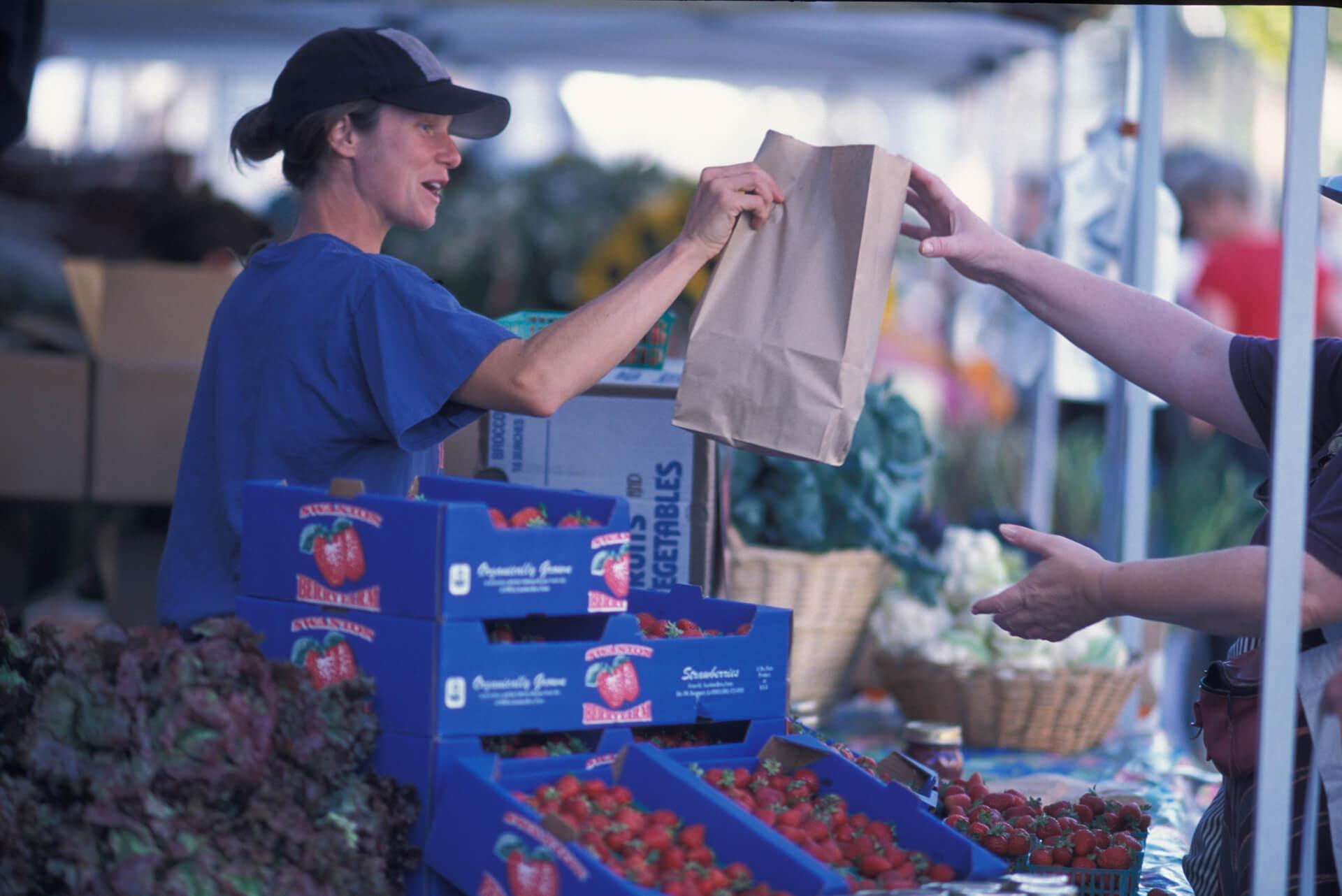 Farmer passing over a paper bag full of produce to a customer at a farmer's market