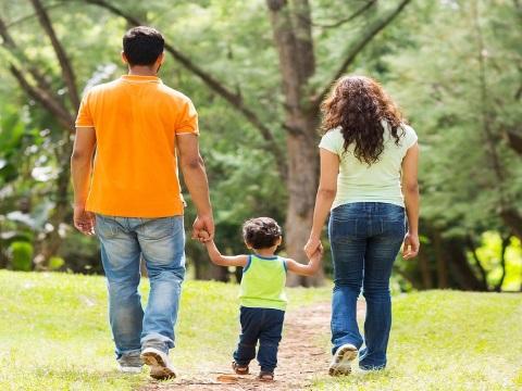 Young family taking a walk on a dirt road towards trees.