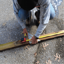 A person is marking wood with a pen and using a measuring tape and a carpenter's square.